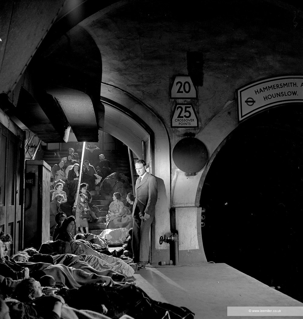 Black and white photo of British artist Henry Moore stood on a London Underground platform, with rows of people taking shelter from the Blitz.