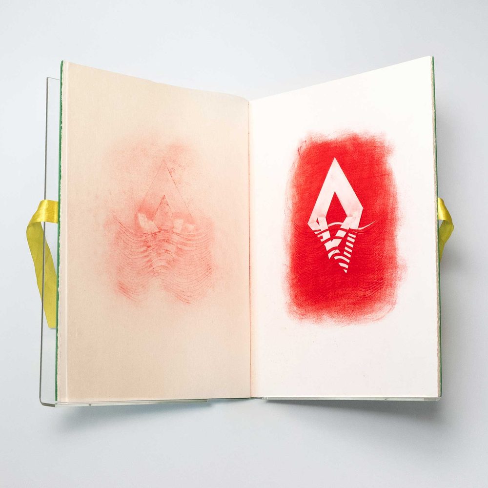 An artist book work. A red, diamond-shaped, abstract image has been stencilled on the right-hand page. On the left, its 'shadow' had transferred to the page.