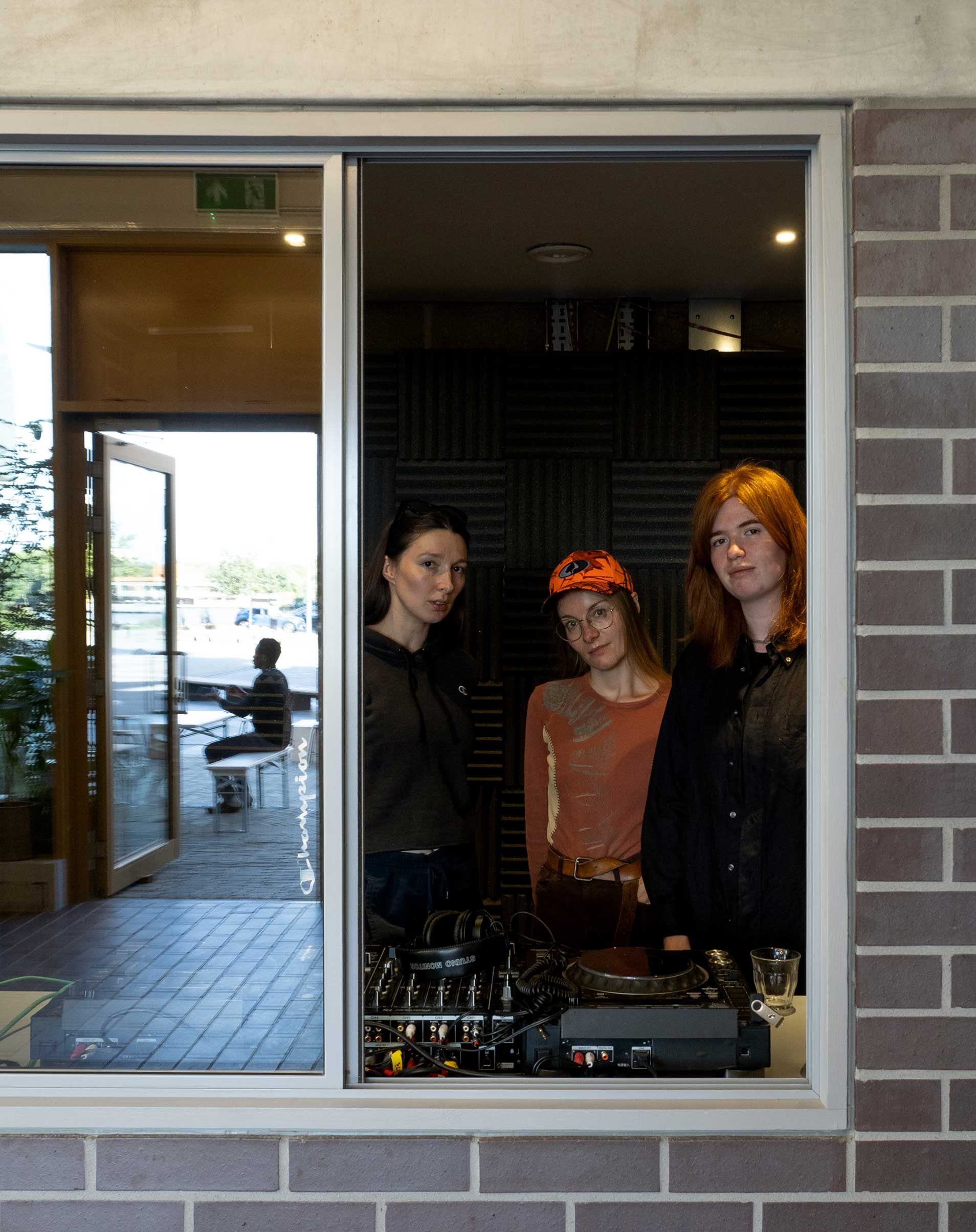 Three people stood in a recording studio, looking out of an open window.