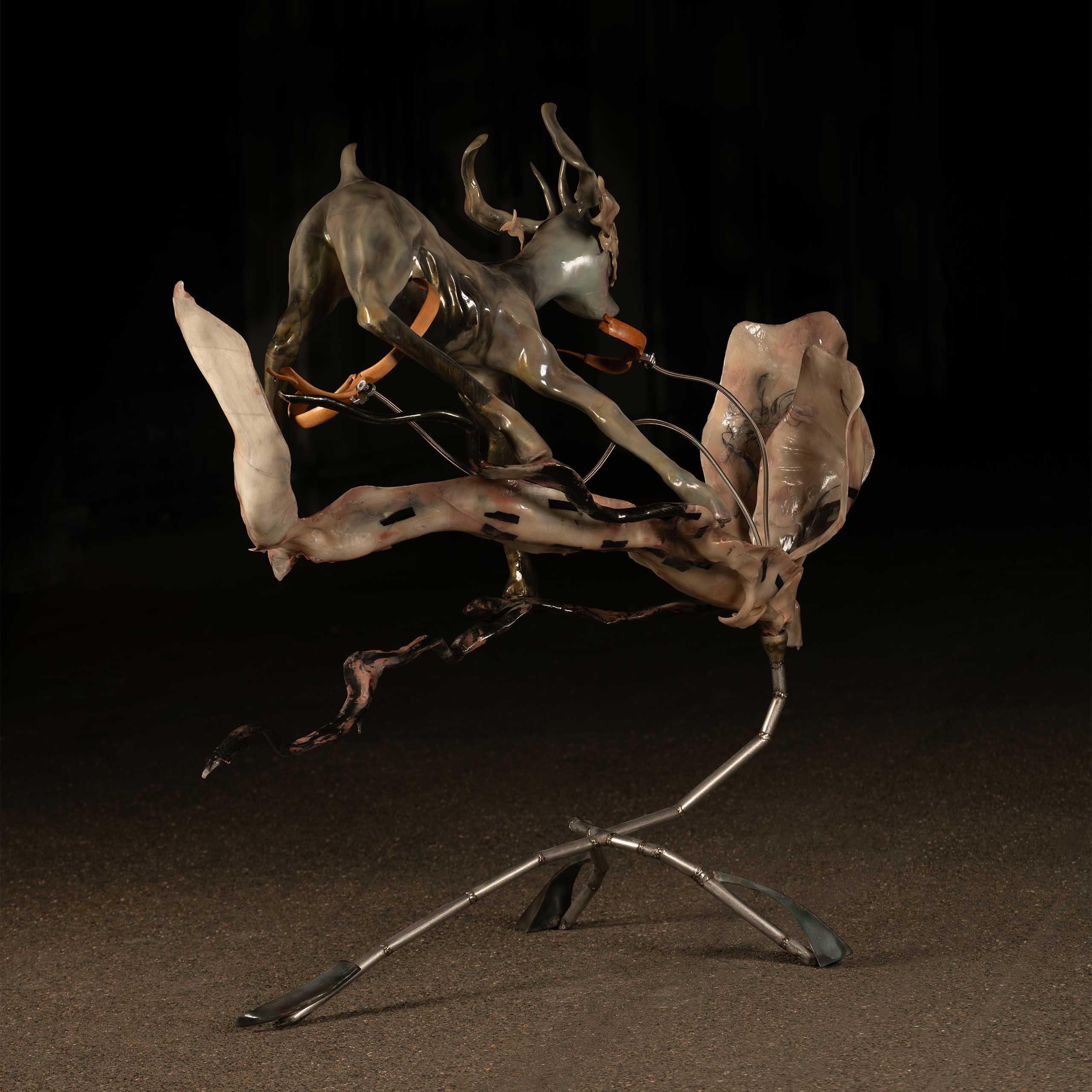 Sculpture of a deer balanced precariously on what looks like a branch or oversized flower, made from metallic components.