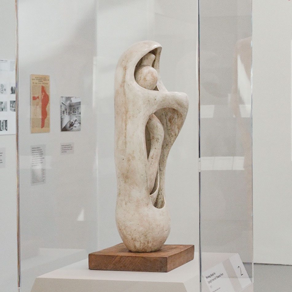 A mid-size sculpture by Henry Moore in white plaster, with a figure-like form embraced or contained by a shell-like outer casing.