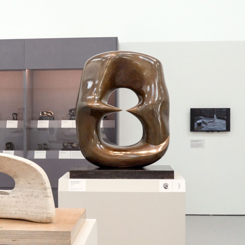 An abstract oval sculpture made of bronze, inside which two points stretch out towards each other, but never quite meet.