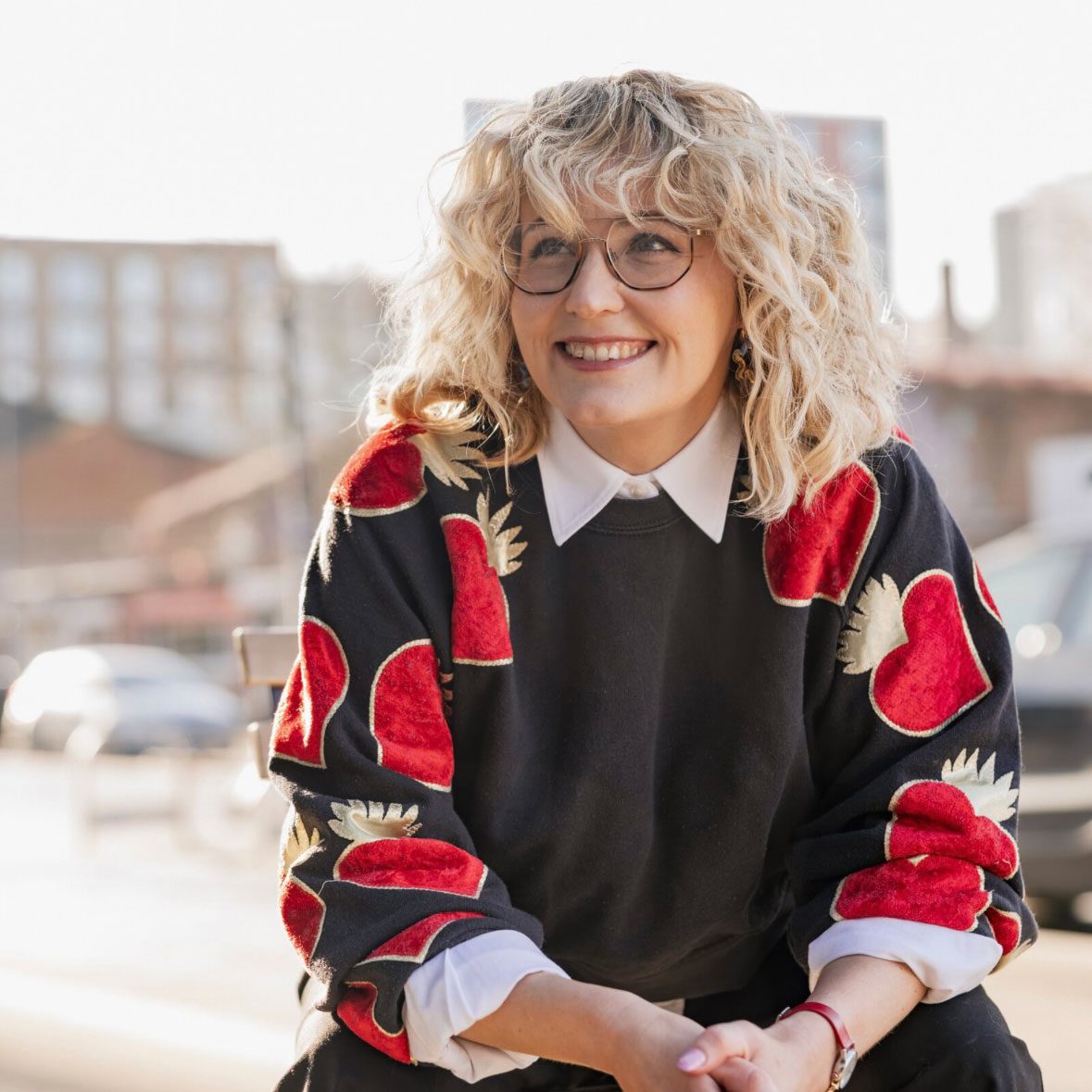 Portrait photo of a smiling woman with curly blonde hair and glasses.